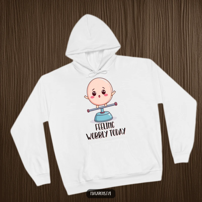 Funny macaron character with surprised expression, balancing on a teeter-totter, cozy hoodie design, lovely funny gift.