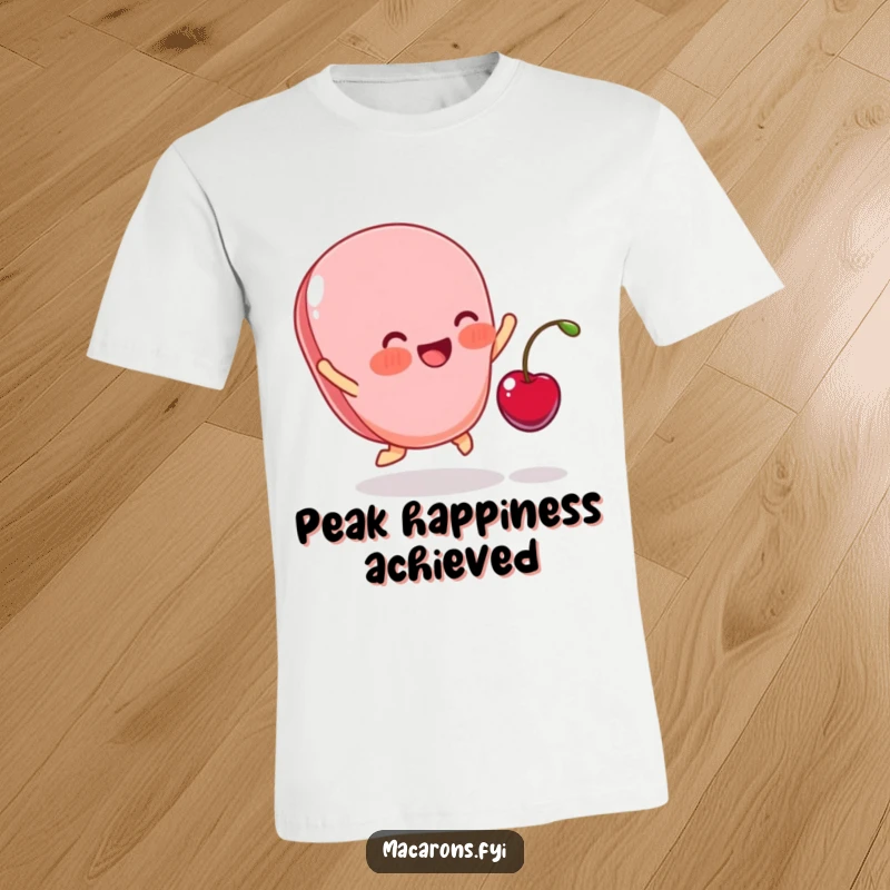 Funny t-shirt featuring a blushing macaron leaping with delight as a tiny cherry lands on its head, celebrating sweet moments.